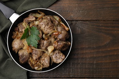 Photo of Pan with tasty fried chicken liver, onion and parsley on wooden table, top view. Space for text