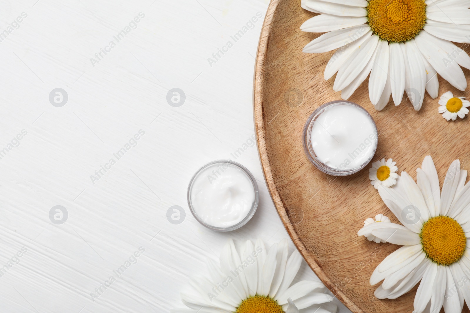 Photo of Flat lay composition with chamomile flowers and cosmetic products on white wooden table, space for text