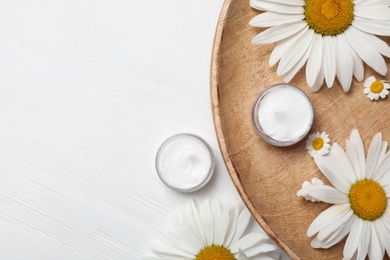 Flat lay composition with chamomile flowers and cosmetic products on white wooden table, space for text