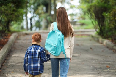 Young mom taking her son to school, back view