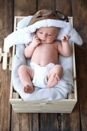 Photo of Cute newborn baby wearing aviator hat in wooden crate, top view