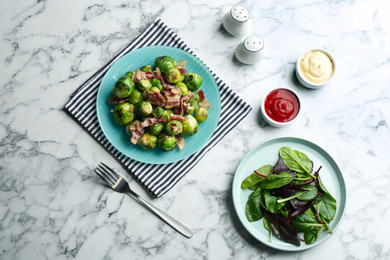 Photo of Delicious Brussels sprouts with bacon on white marble table, flat lay