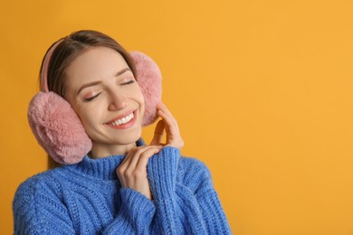 Happy woman wearing warm earmuffs on yellow background, space for text