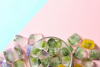 Photo of Ice cubes with flowers and glass bowl on color background, flat lay. Space for text