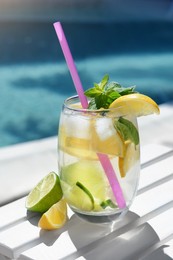Refreshing water with lemon slices and mint on white wooden table near swimming pool