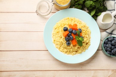 Plate with tasty millet porridge, blueberries, pumpkin and mint on light wooden table, flat lay. Space for text