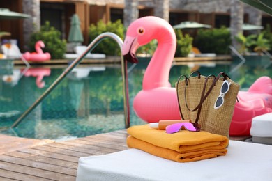 Beach accessories on sun lounger and float in shape of flamingo near outdoor swimming pool, space for text. Luxury resort