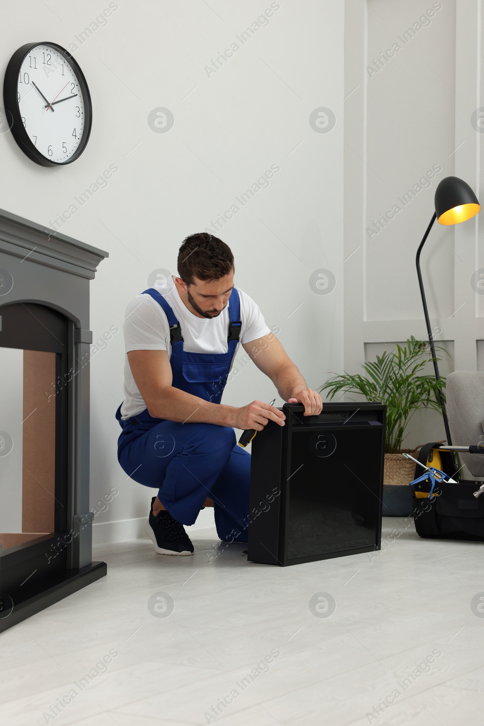 Photo of Professional technician with screwdriver installing electric fireplace in room