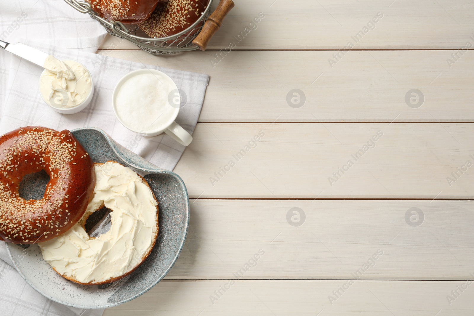 Photo of Delicious bagel with cream cheese and coffee on white wooden table, flat lay. Space for text