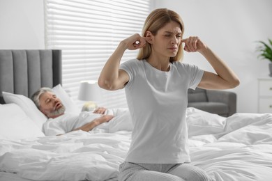 Photo of Irritated woman covering her ears in bed at home. Problem with snoring husband