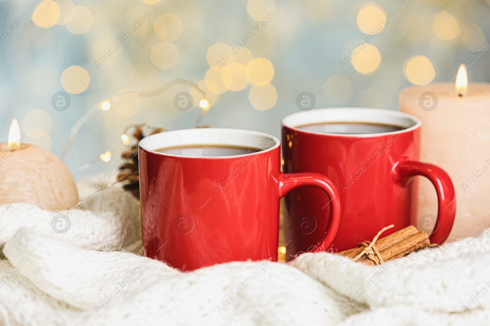 Photo of Cups of hot winter drink and burning candles on knitted plaid against blurred lights