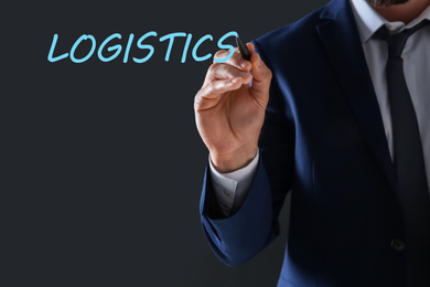 Businessman pointing at word LOGISTICS on virtual screen against dark background, closeup 