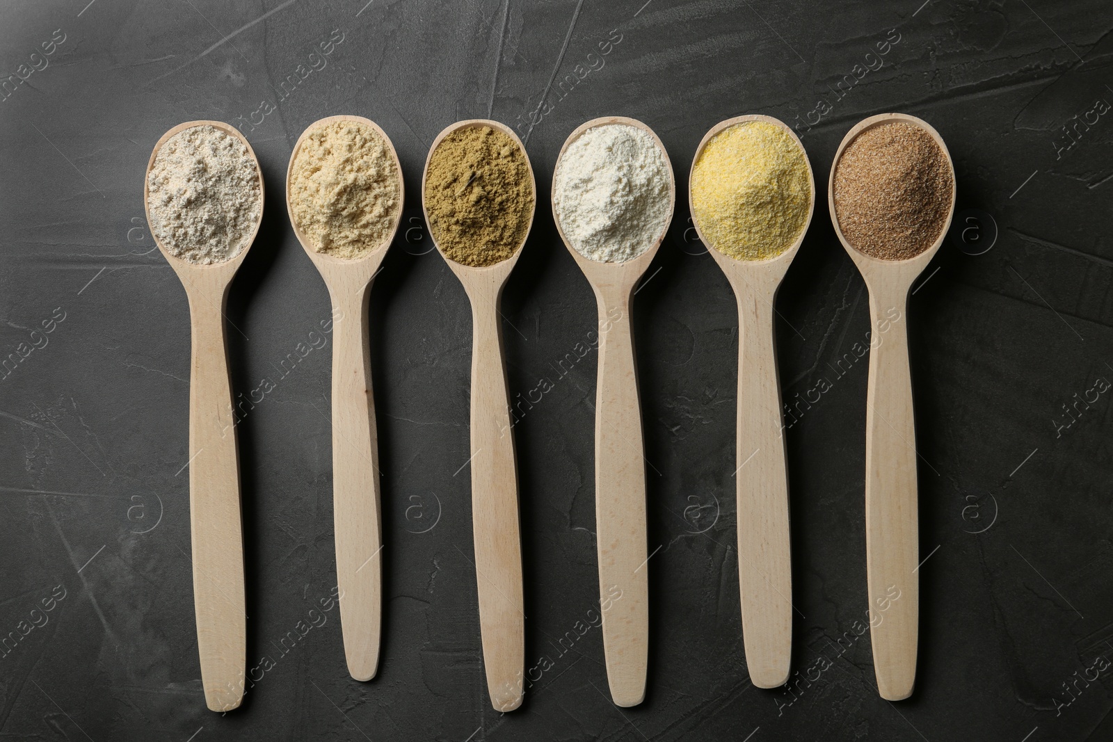 Photo of Spoons with different types of flour on grey background, top view