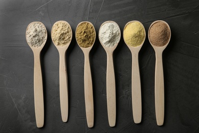 Spoons with different types of flour on grey background, top view