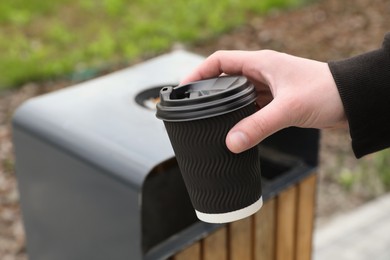 Photo of Man throwing black paper cup into trash can outdoors, closeup. Space for text