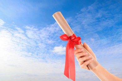 Image of Graduated student holding diploma against blue sky on sunny day, closeup