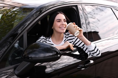 Photo of Young woman with cup of coffee sitting inside her modern car