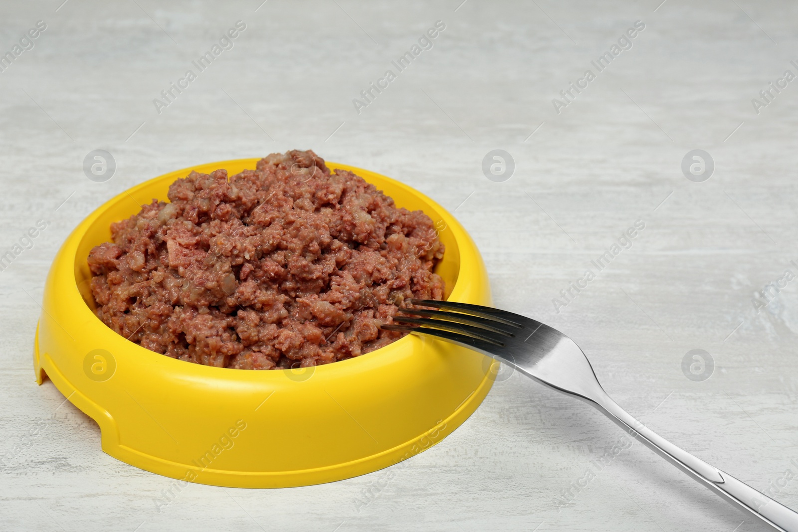 Photo of Bowl of wet pet food with fork on white table