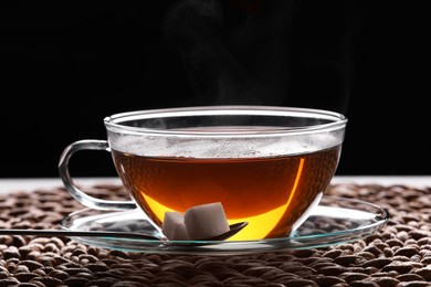 Glass cup of tea with sugar cubes on table against black background, closeup
