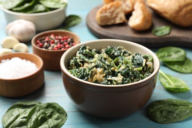 Photo of Tasty spinach dip with egg in bowl and spices on light blue wooden table, closeup