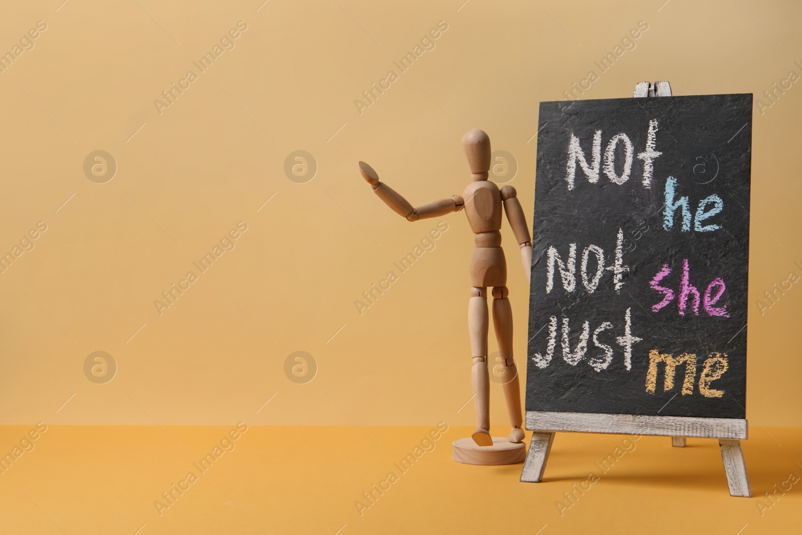 Photo of Chalkboard with text Not he, not she, just me and mannequin on pale orange background. Gender identity