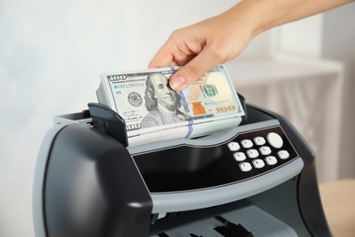 Photo of Woman putting money into counting machine indoors, closeup