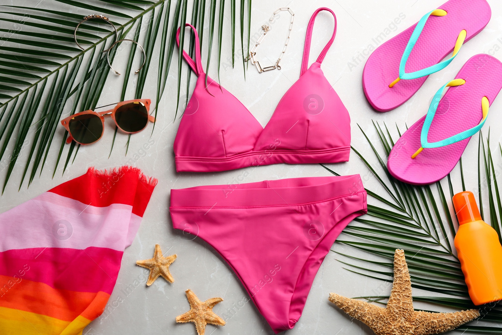 Photo of Beautiful pink bikini and beach accessories on light marble background, flat lay