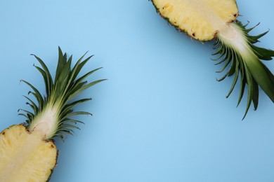 Halves of ripe pineapple on light blue background, flat lay. Space for text