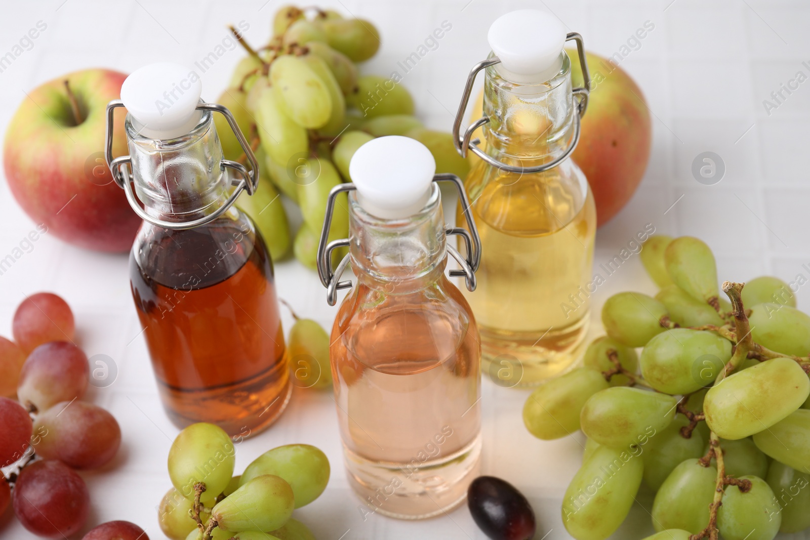 Photo of Different types of vinegar and ingredients on light tiled table, closeup