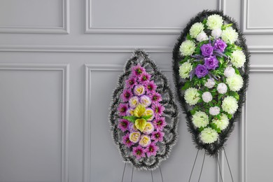 Funeral wreaths of plastic flowers near light grey wall, space for text