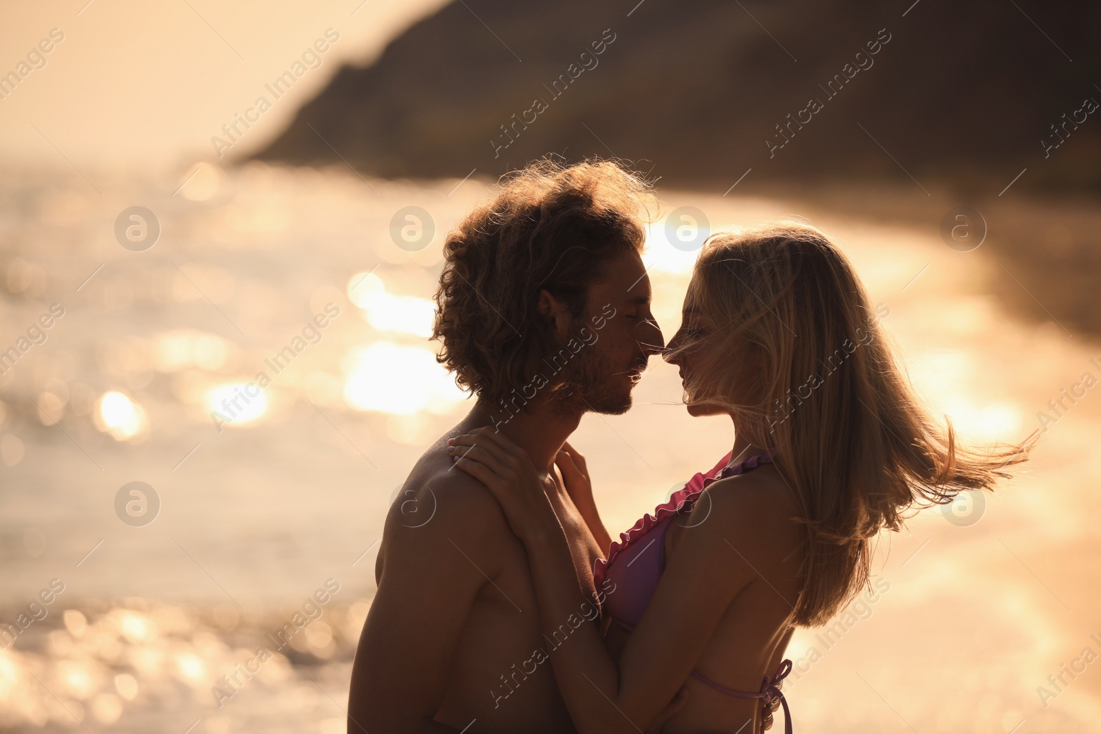 Photo of Young woman in bikini kissing her boyfriend on beach at sunset. Lovely couple