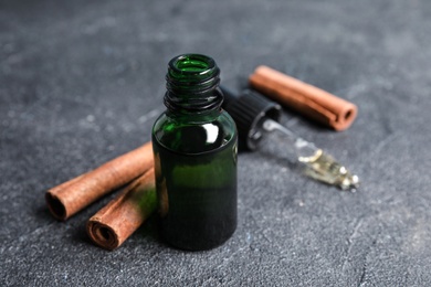 Photo of Bottle of essential oil and cinnamon sticks on grey table