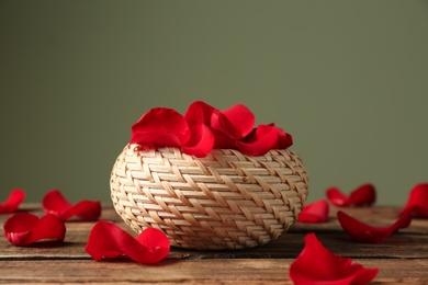 Photo of Wicker basket with rose petals on table against color background