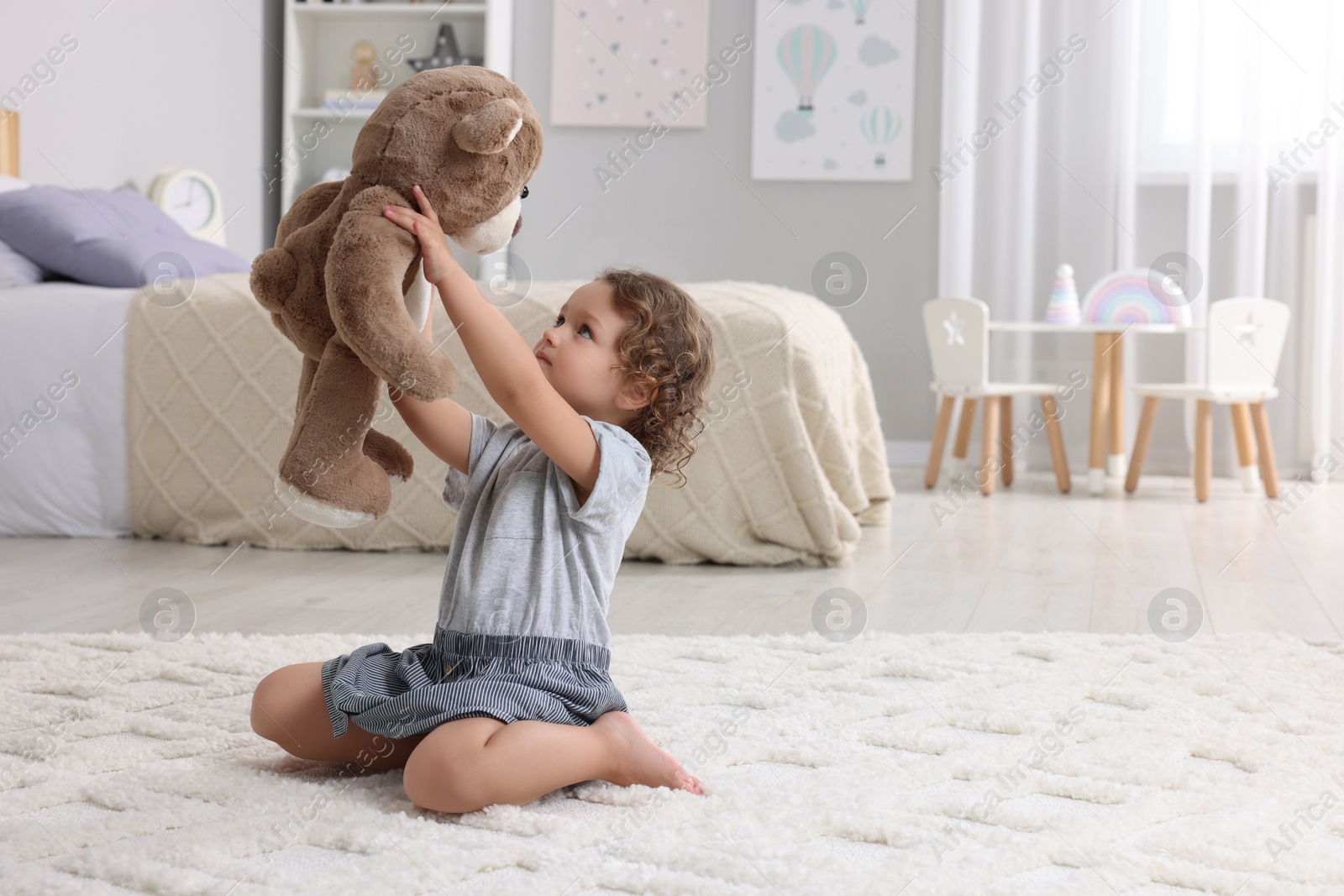 Photo of Cute little girl playing with teddy bear on floor at home