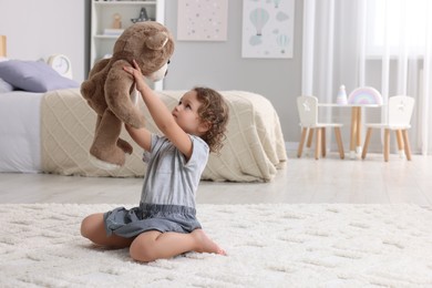Photo of Cute little girl playing with teddy bear on floor at home