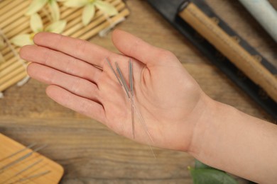 Photo of Woman holding many acupuncture needles over wooden table, closeup