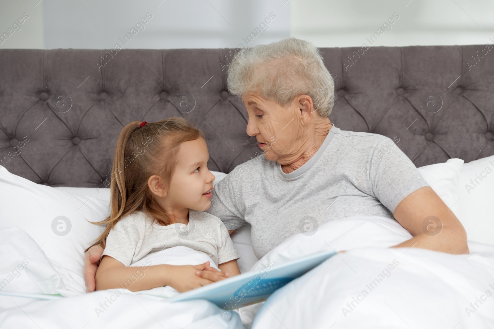 Photo of Cute girl and her grandmother reading book on bed at home