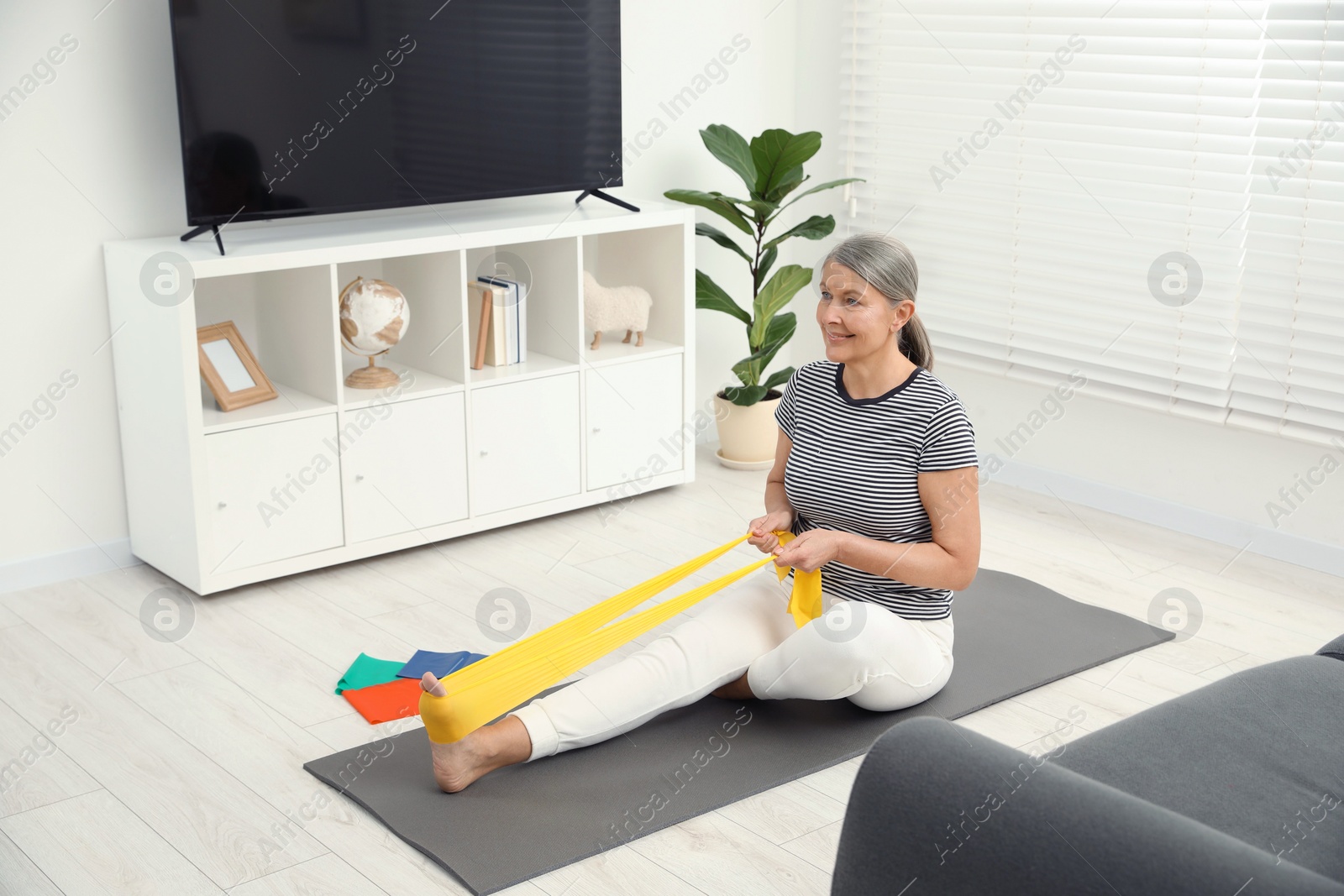 Photo of Senior woman doing exercise with fitness elastic band on mat at home