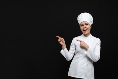 Photo of Happy female chef pointing at something on black background. Space for text