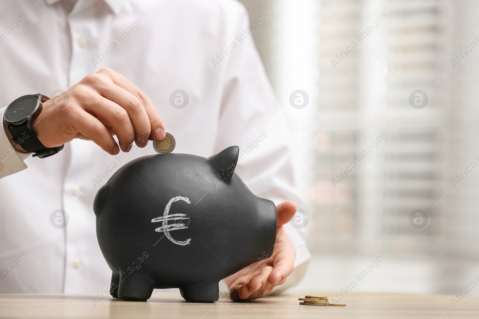 Photo of Man putting coin into piggy bank with euro sign at wooden table, closeup. Space for text