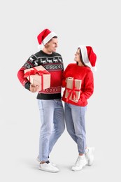 Photo of Beautiful happy couple in Santa hats holding Christmas gifts on light background