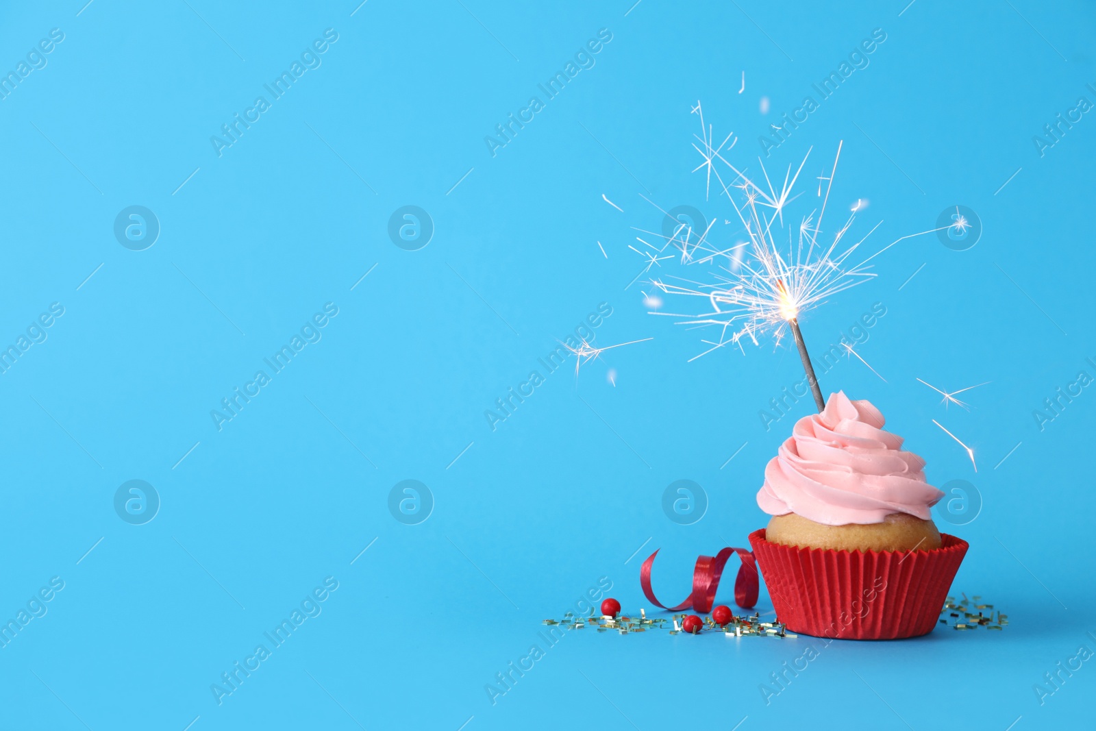 Photo of Birthday cupcake with burning sparkler on light blue background. Space for text