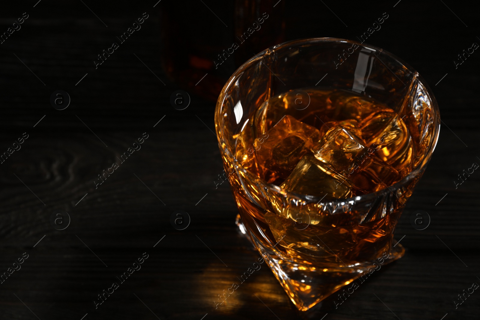 Photo of Golden whiskey in glass with ice cubes on table. Space for text