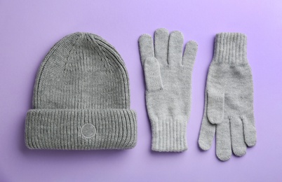 Woolen gloves and hat on violet background, flat lay