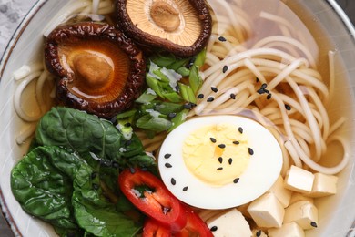Photo of Delicious vegetarian ramen with egg, mushrooms, tofu and vegetables in bowl, top view. Noodle soup