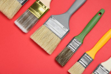 Photo of Many different paint brushes on red background, flat lay