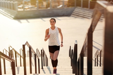 Photo of Sporty young woman running upstairs on sunny day