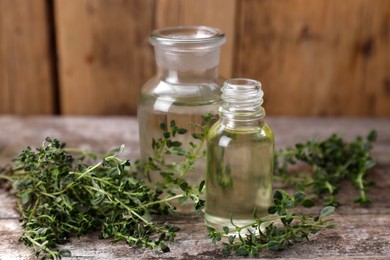 Photo of Bottles of thyme essential oil and fresh plant on wooden table