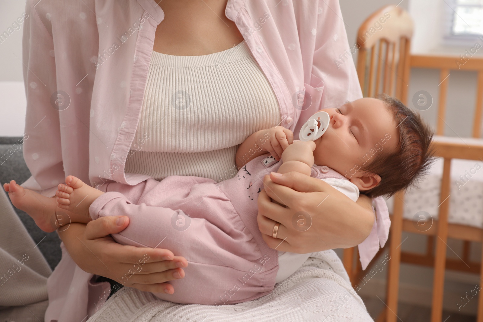 Photo of Mother holding her cute little baby with pacifier at home, closeup