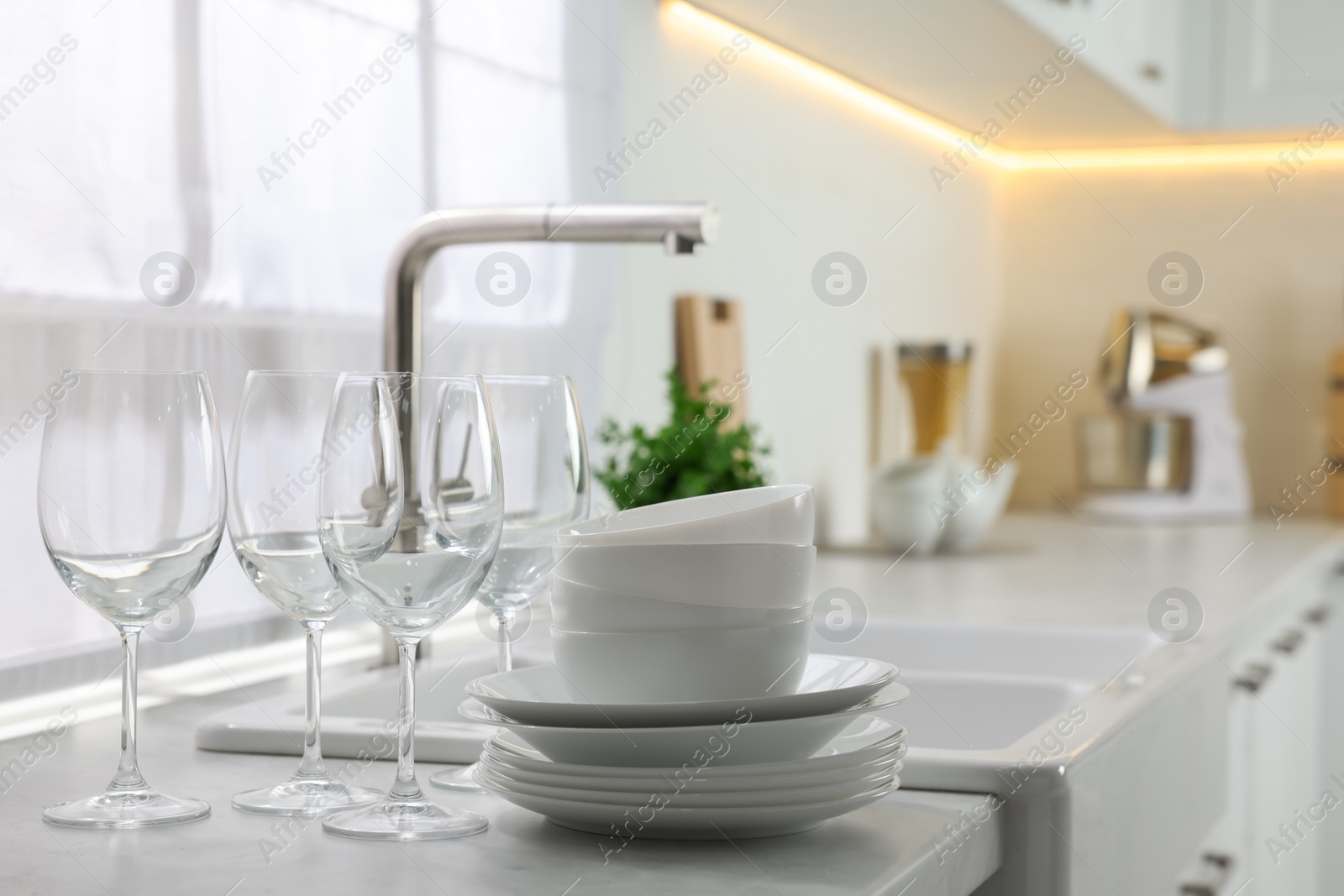 Photo of Different clean dishware and glasses on countertop near sink in kitchen